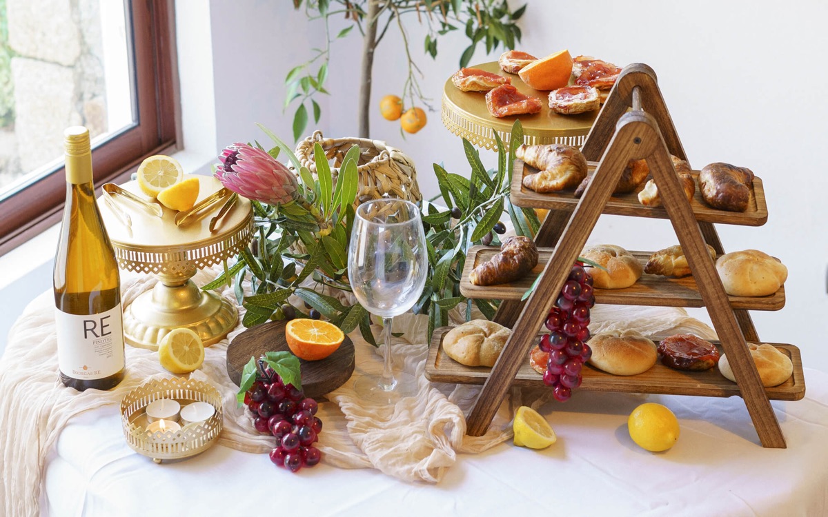 Montaje de Casa Oliva en un matrimonio: torre de madera con bollería, frutas, vino y flores